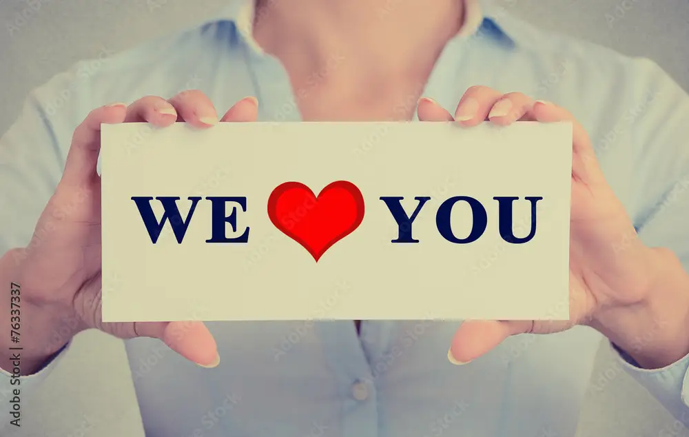 Person holding a sign that says 'We ❤️ You' with bold text and a red heart symbol.