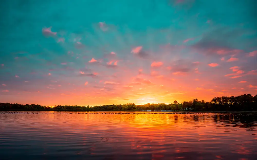 Tranquil sunset over a Minnesota lake, with the vivid blue sky transitioning from vibrant orange to deep purple hues.