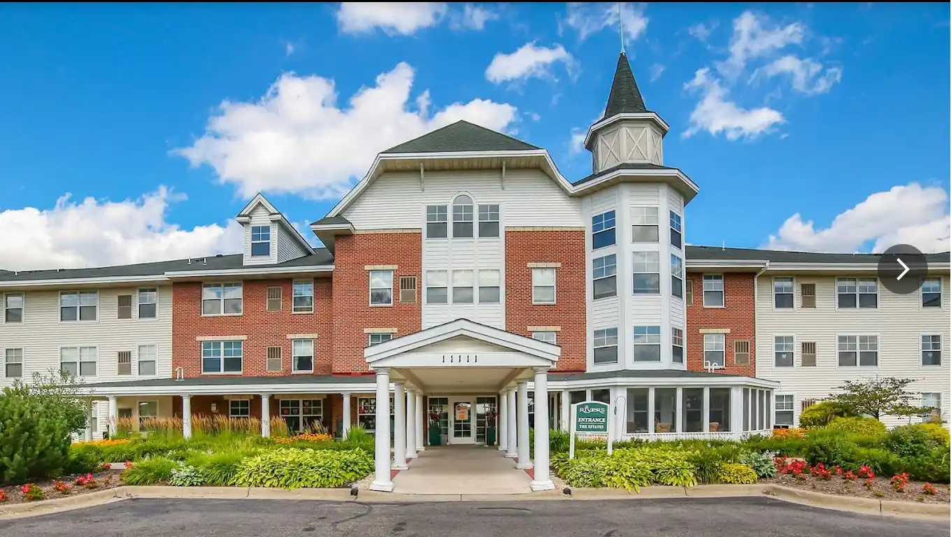 Front entrance of The Rivers senior living community in Burnsville, Minnesota, featuring brick facade, white columns, and landscaped gardens.